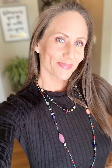A woman wearing a black sweater and a long necklace is taking a selfie.
