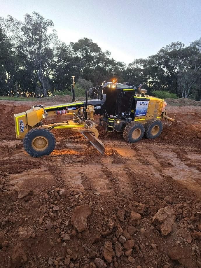 A Motor Grader Levels Red Dirt in A Construction Site at Dusk — One Group Industries Pty Ltd in Bathurst, NSW