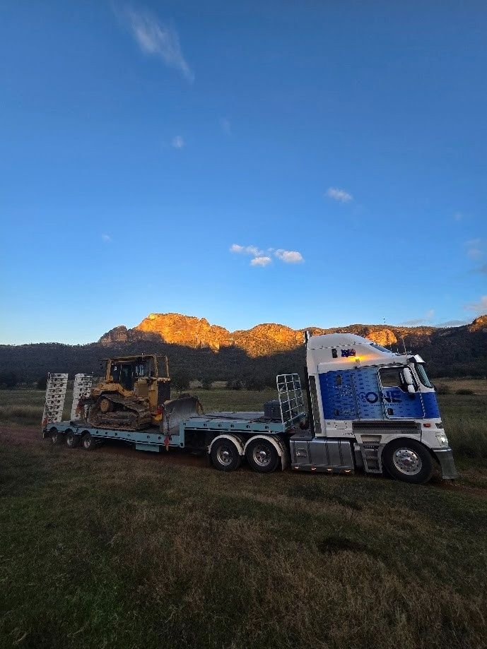 A Bulldozer on A Flatbed Trailer Through a Grassy Field — One Group Industries Pty Ltd in Bathurst, NSW