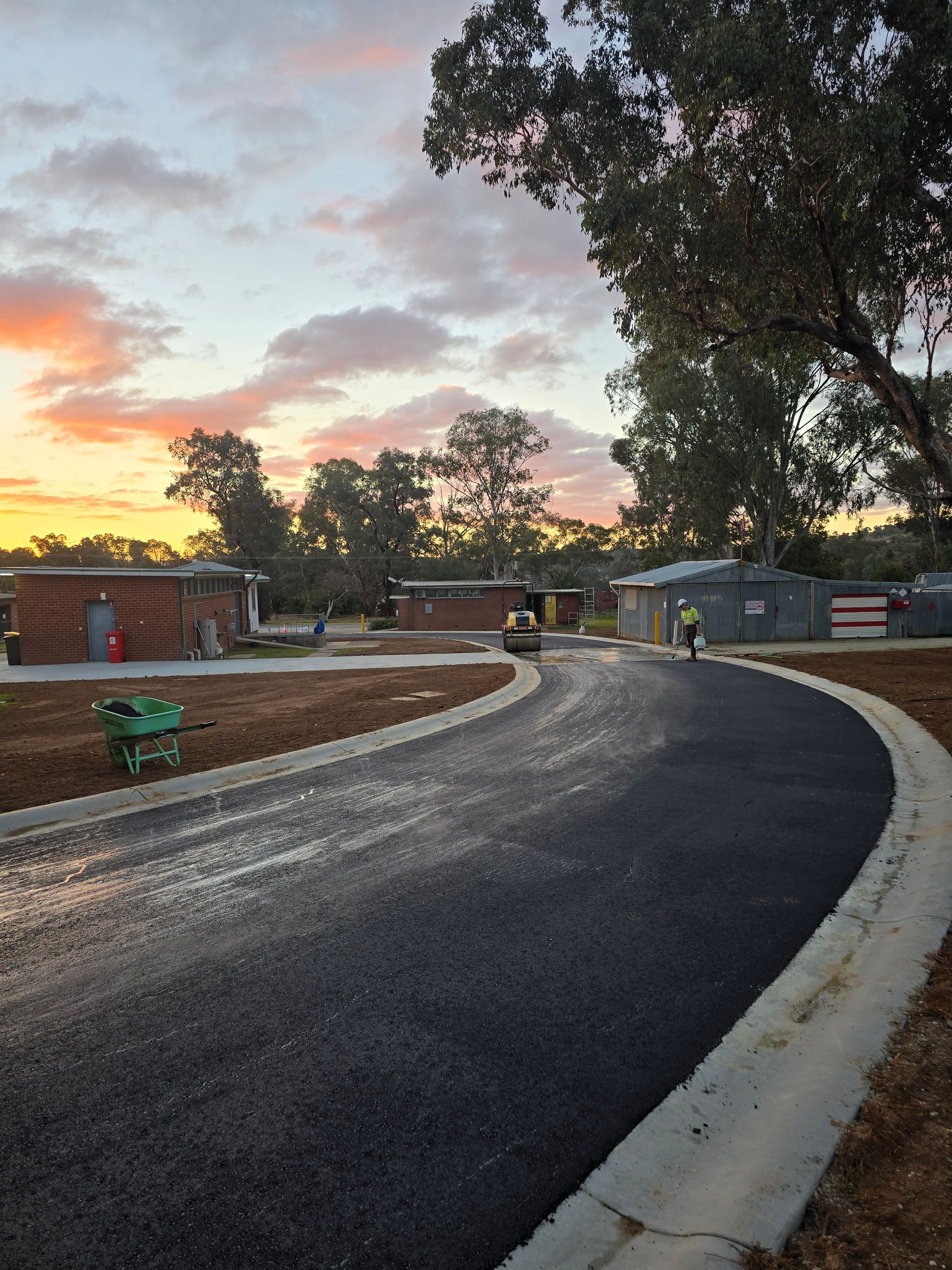 Paved road curves through a construction site at sunset. Workers and buildings are visible — One Group Industries Pty Ltd in Bathurst, NSW
