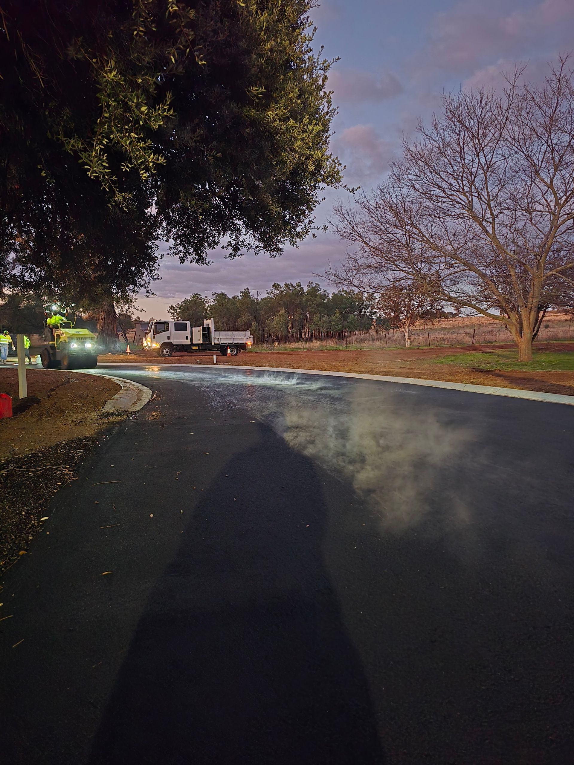 Paved road at dusk with a car and trees in the background — One Group Industries Pty Ltd in Bathurst, NSW