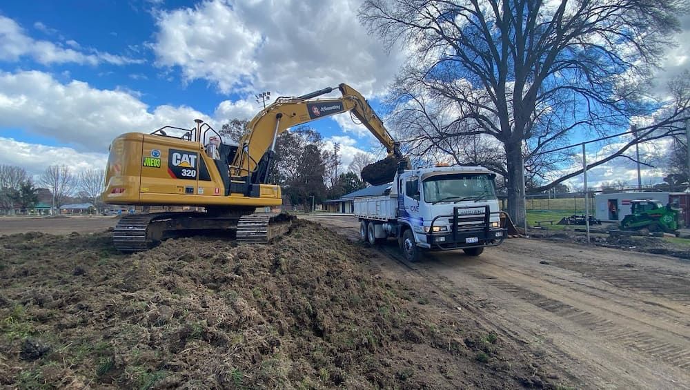 A Large Excavator is Loading Dirt Into a Dump Truck — One Group Industries Pty Ltd in Bathurst, NSW
