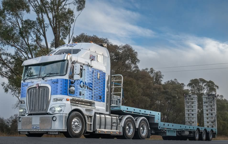 A large white and blue semi-truck with an empty flatbed trailer on a road — One Group Industries Pty Ltd in Bathurst, NSW