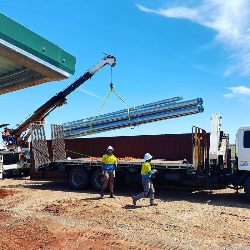 Crane lifting metal beams onto a truck bed; two workers in yellow vests — One Group Industries Pty Ltd in Bathurst, NSW