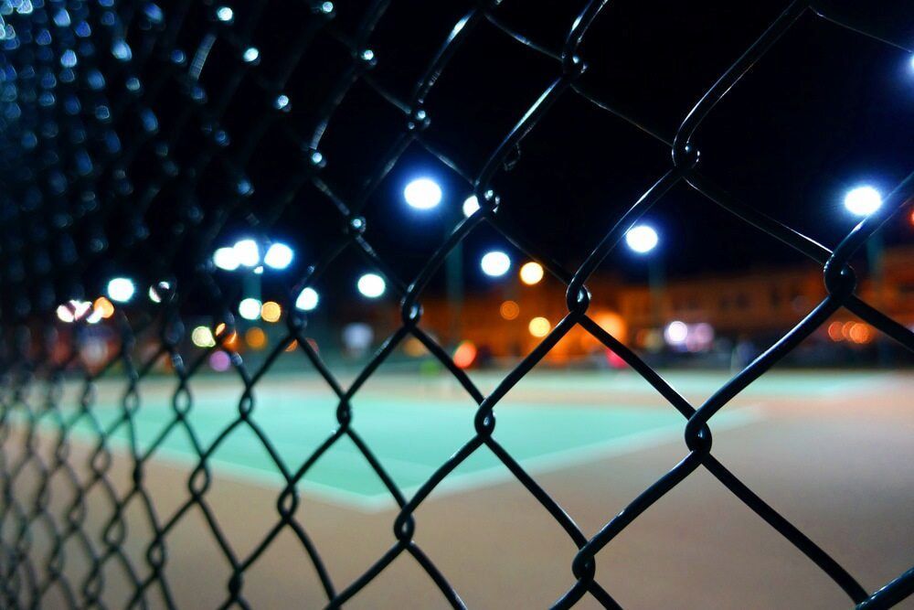 A Tennis Court is Behind a Chain Link Fence at Night — One Group Industries Pty Ltd in Bathurst, NSW