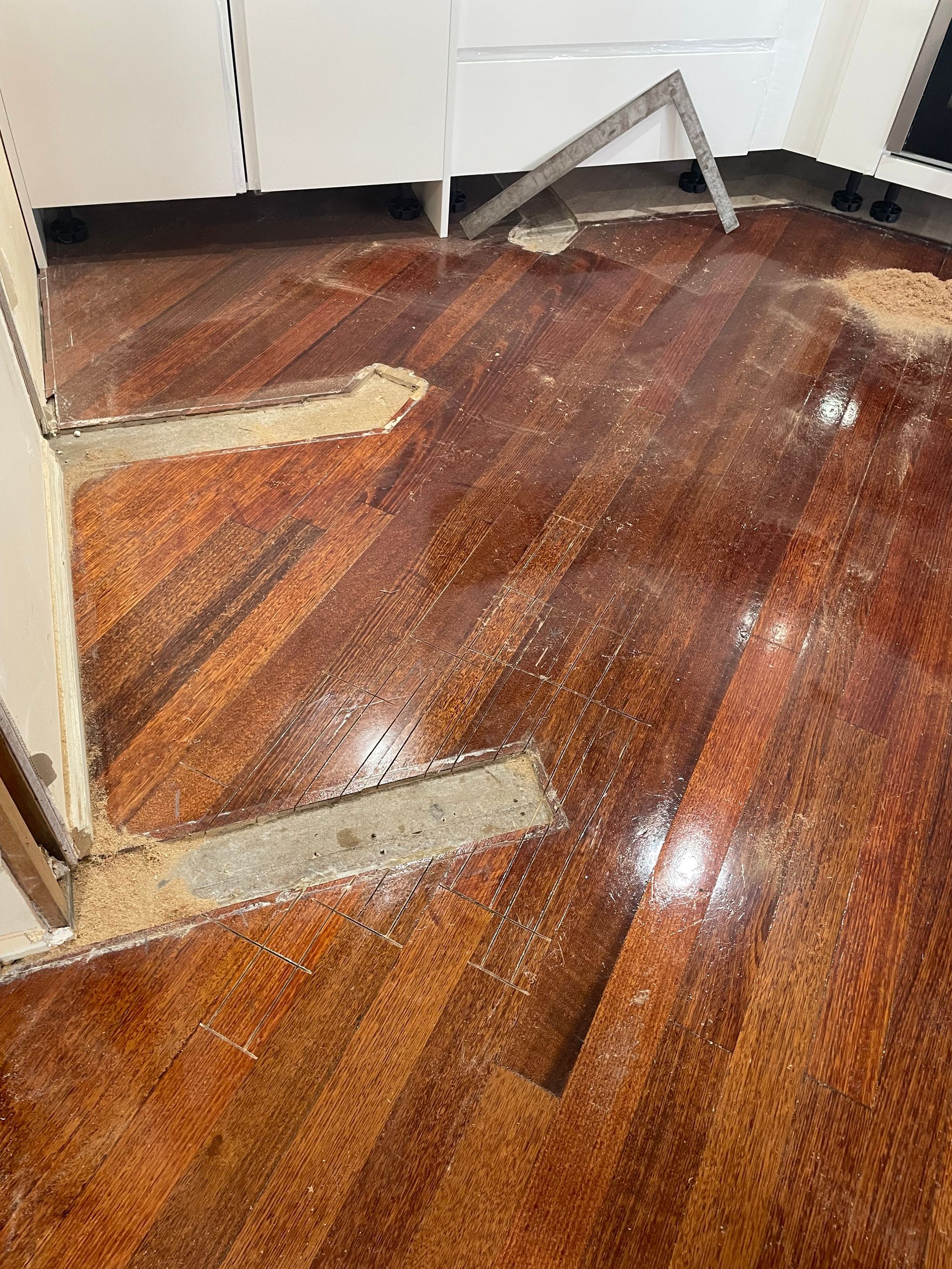 Water-damaged hardwood floor with lifted boards and exposed patches near a white wall — Finer Floors In Cambridge, TAS