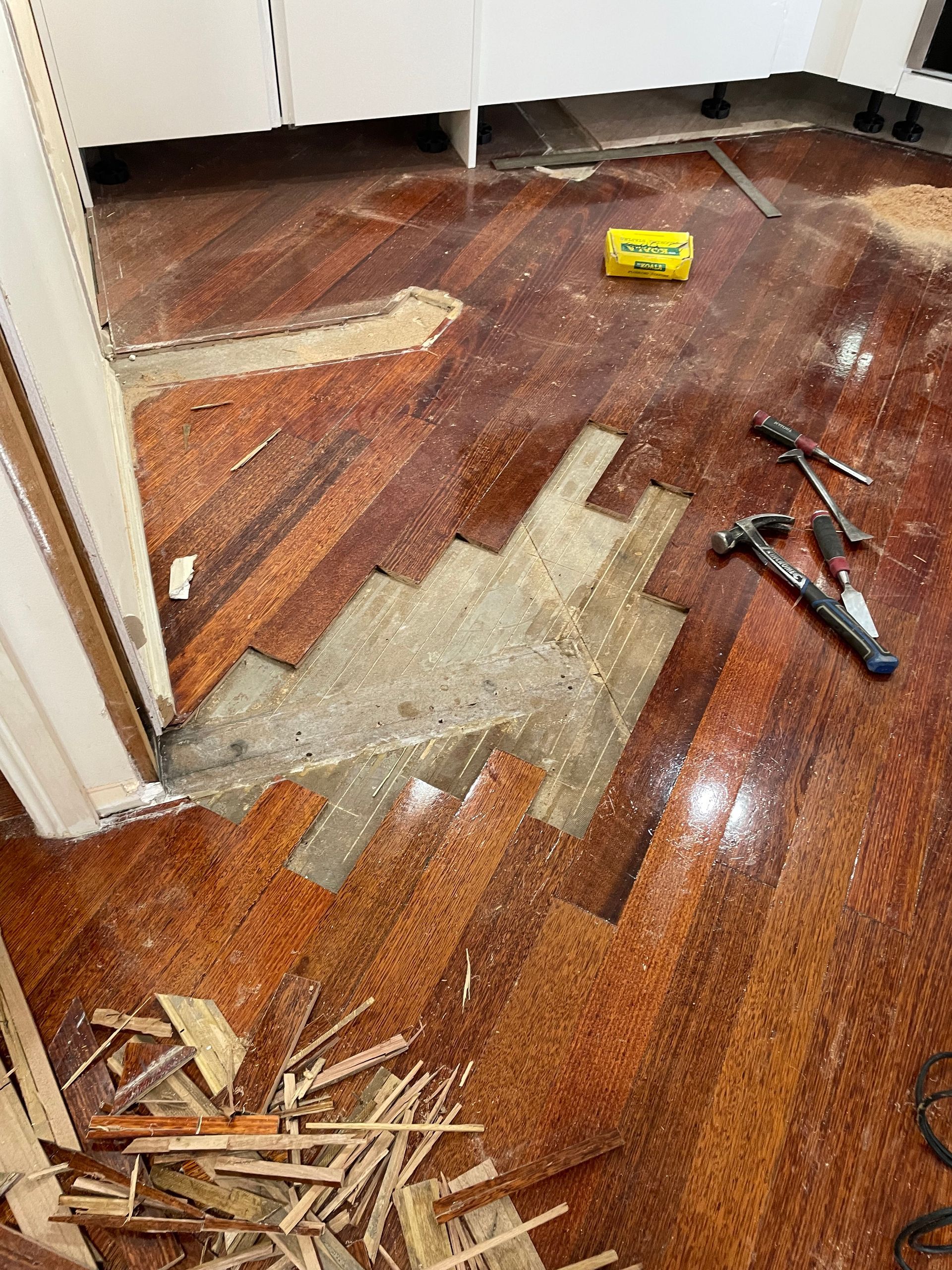 Damaged hardwood floor with patches of missing wood and scattered tools in a room under repair — Finer Floors In Cambridge, TAS