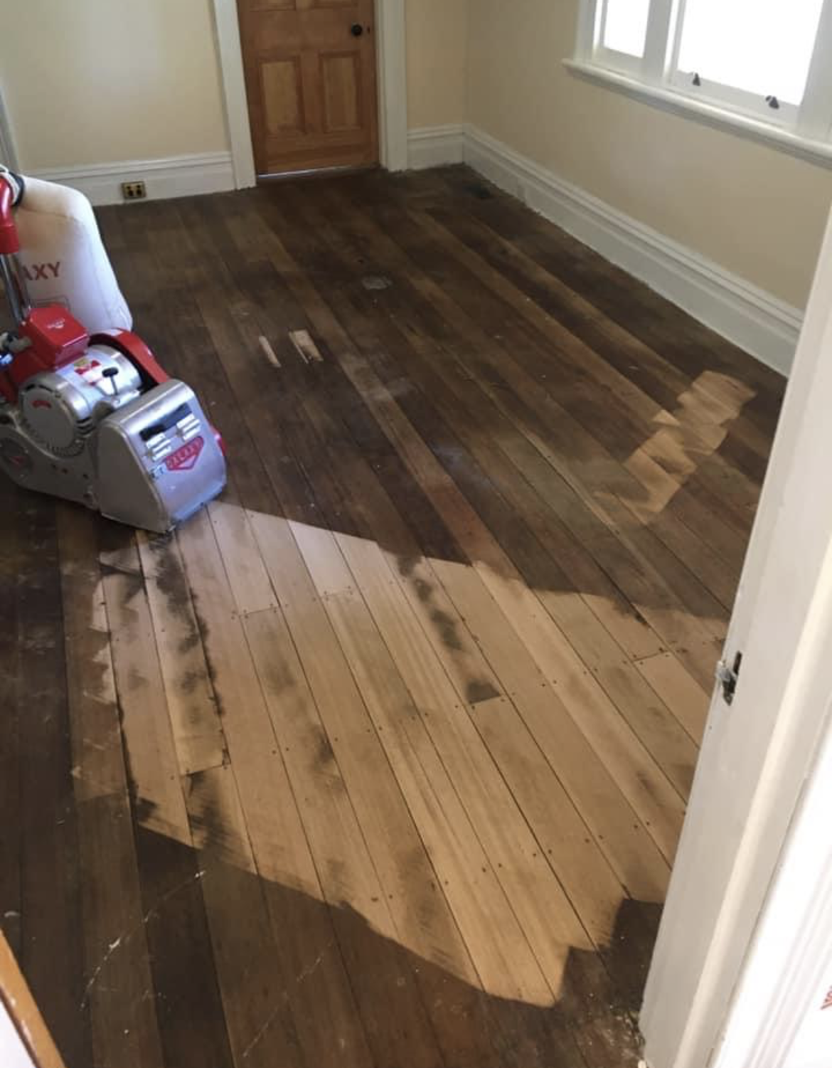 Damaged wood floor with a large stripped section in a small room with a vacuum and cleaning supplies. — Finer Floors In Cambridge, TAS