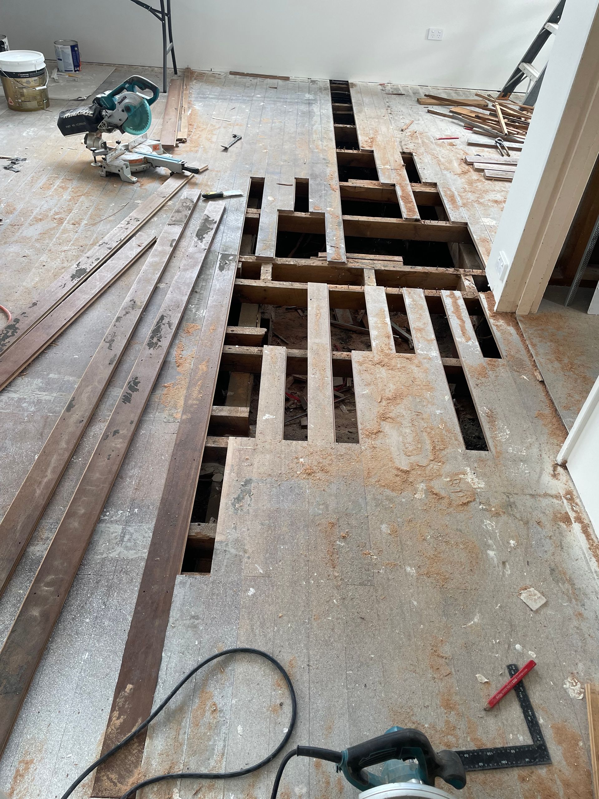 Damaged floor with large cut-out sections, tools, and wood planks in a renovation area — Finer Floors In Cambridge, TAS