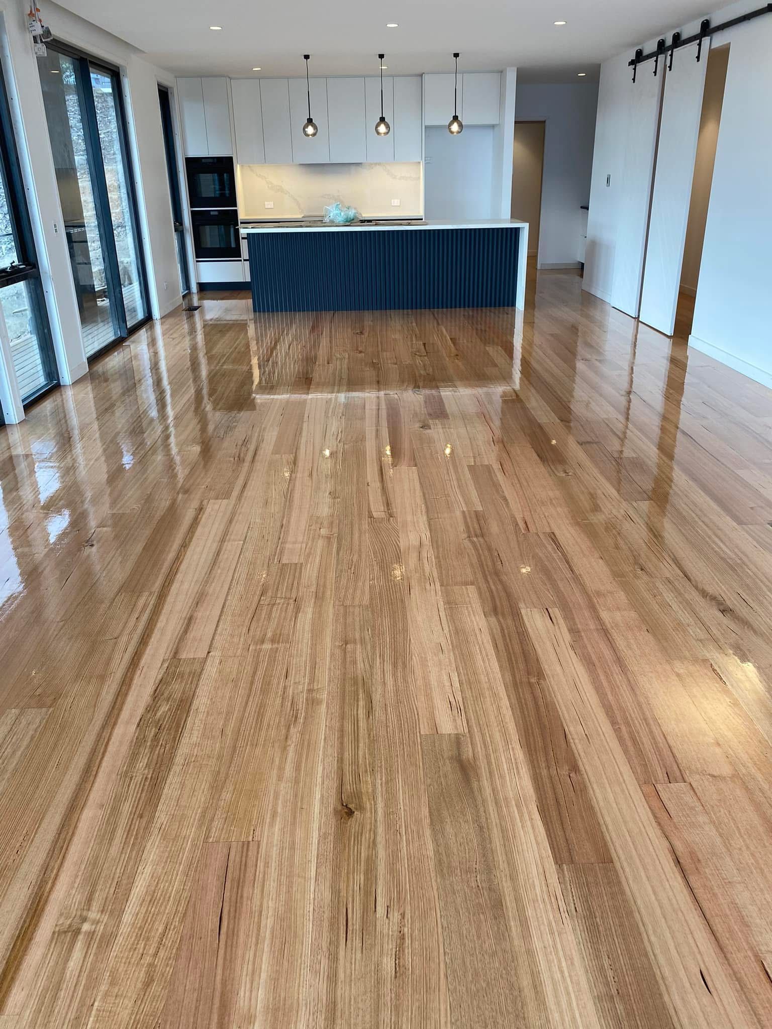 Bright empty room with glossy wood floors, kitchen island, and large windows. — Finer Floors In Cambridge, TAS