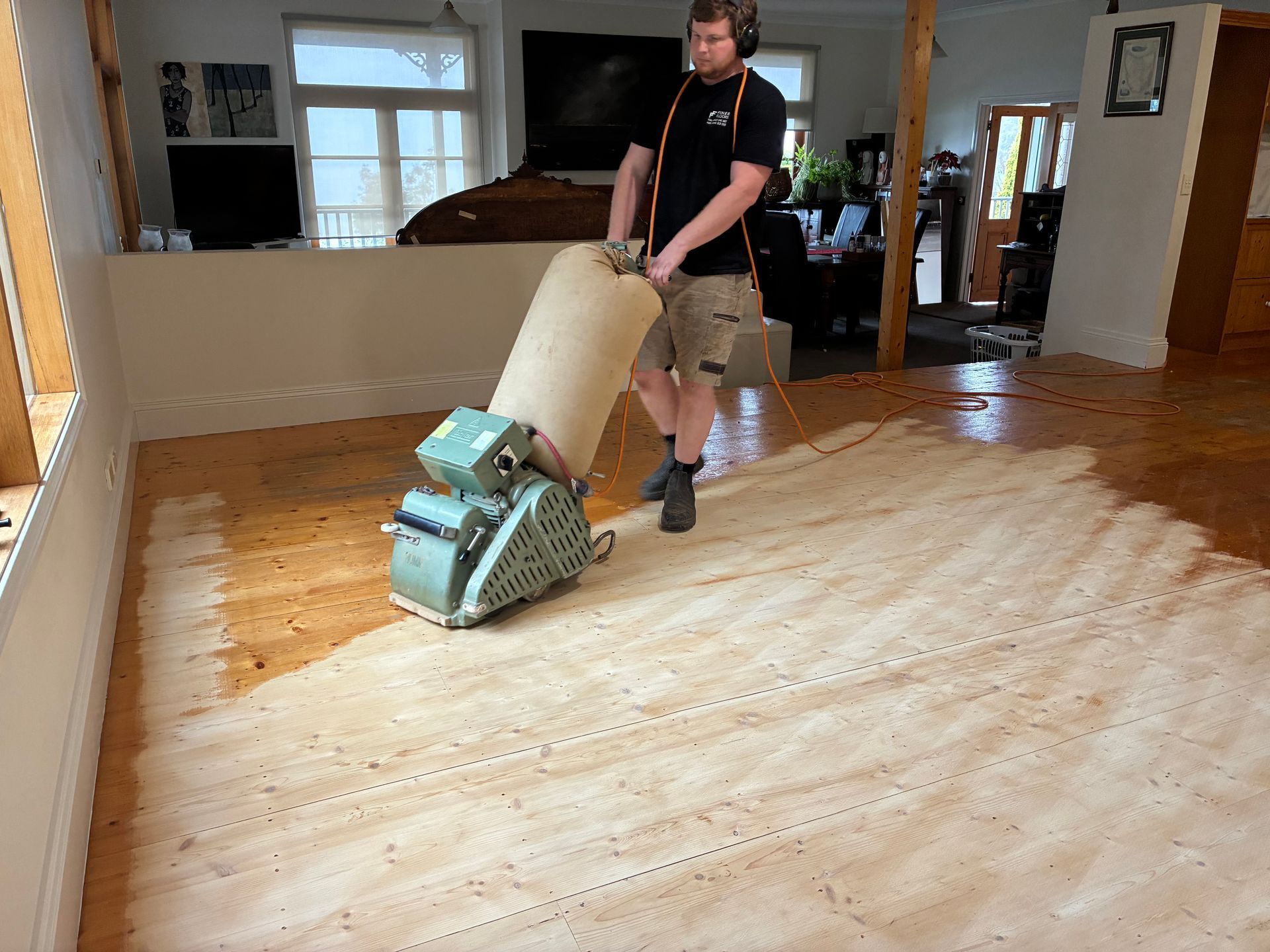 Person operating a floor sander on a partially refinished hardwood floor indoors — Finer Floors In Cambridge, TAS