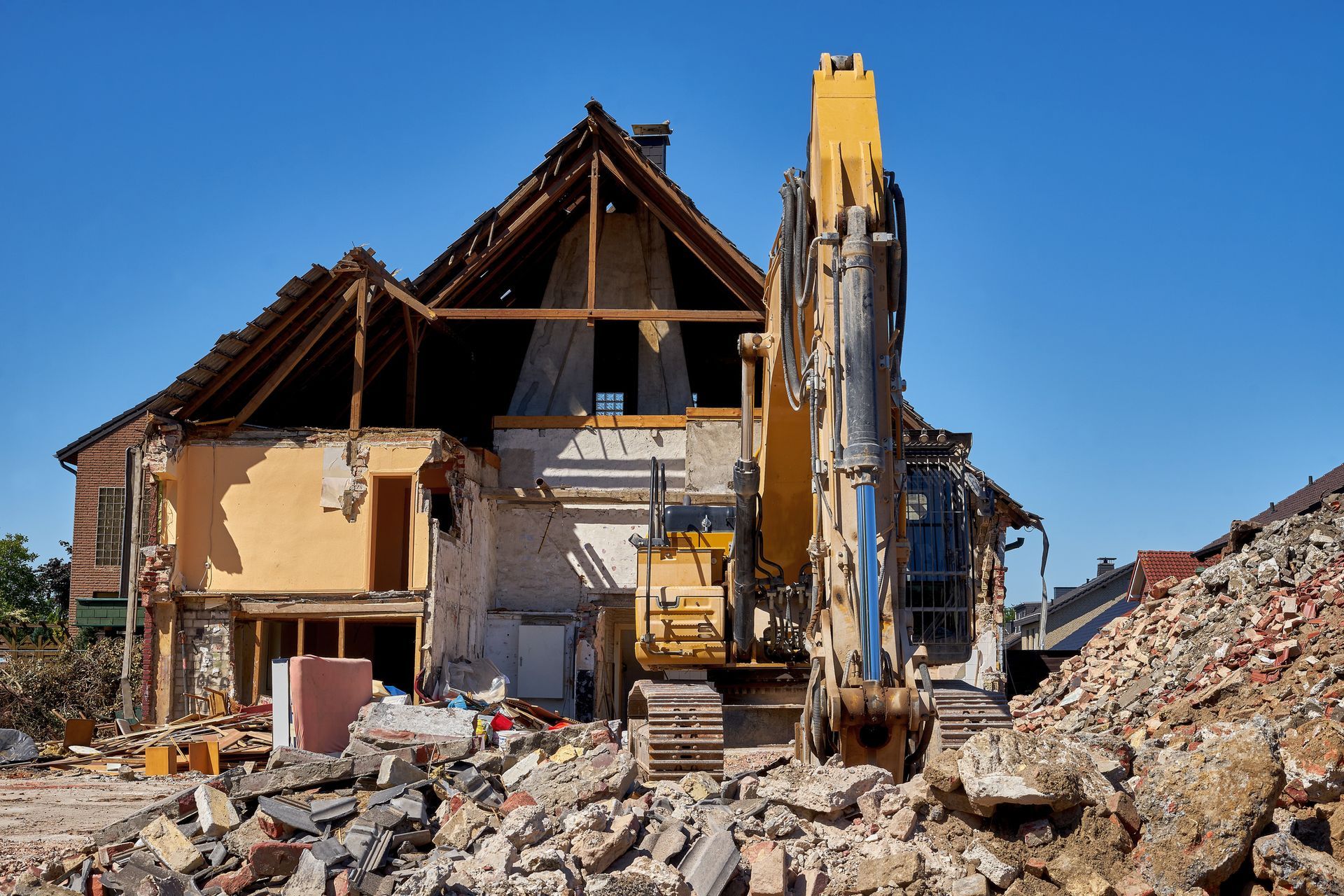Casa demolita con una ruspa tra le macerie, sotto un cielo azzurro e terso
