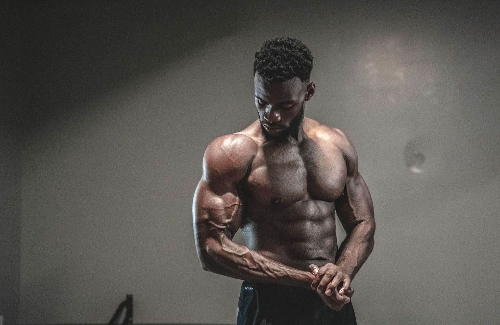 Muscular person flexing arm, indoors with dark, neutral background.