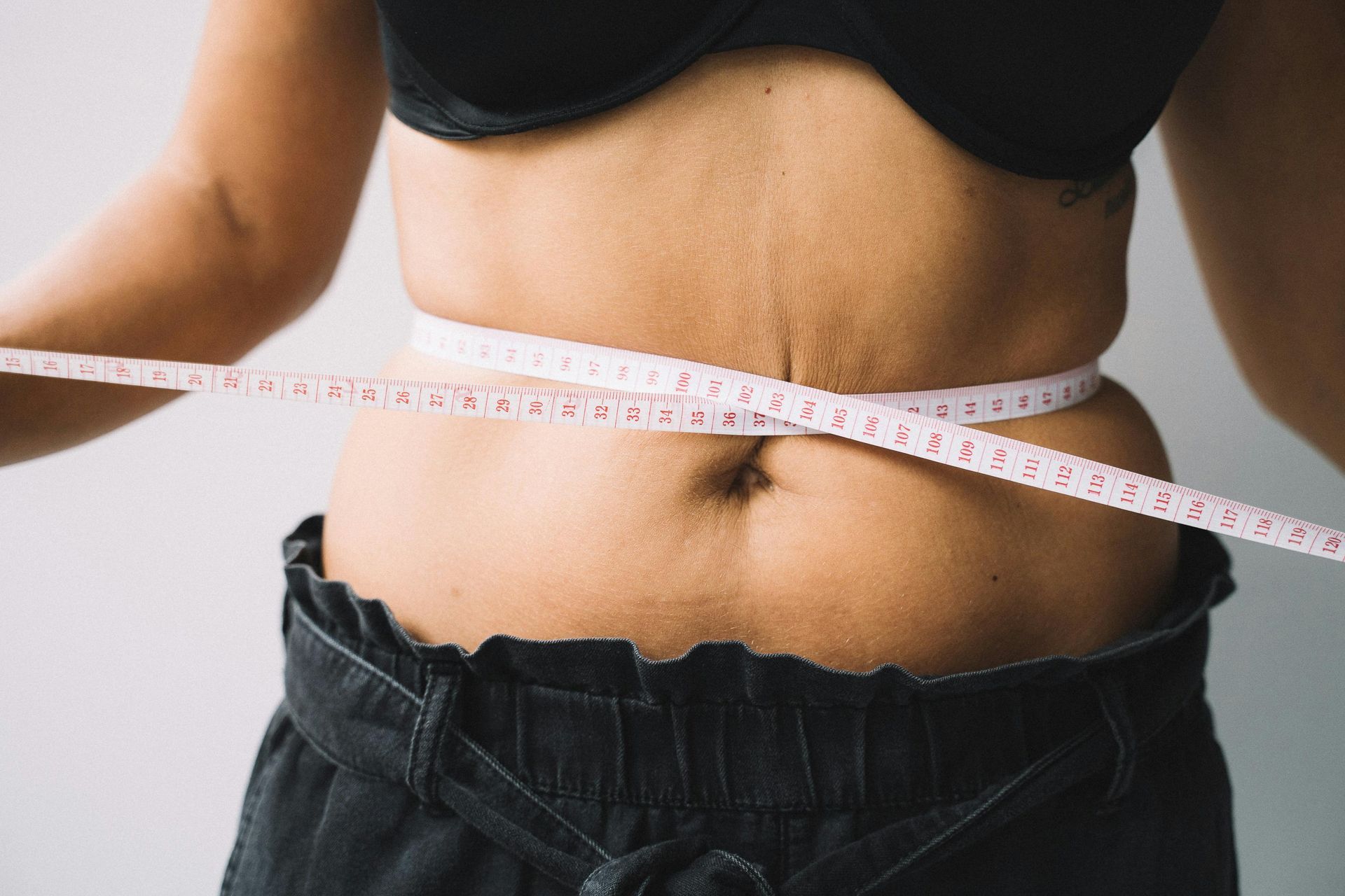 A person's torso with a measuring tape around the waist, wearing a black bra and black pants.