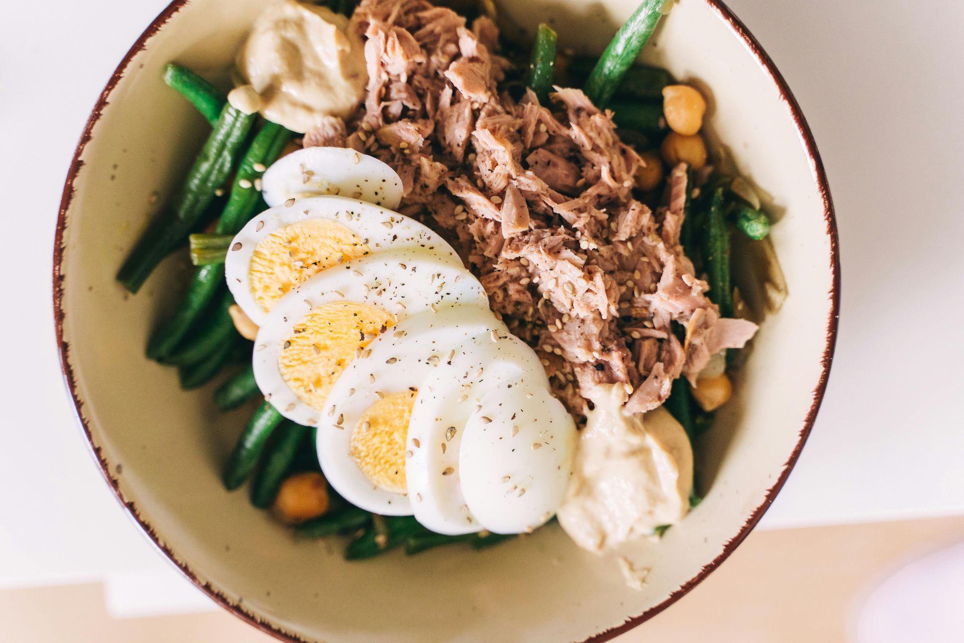 Salad bowl with green beans, tuna, sliced eggs, chickpeas, and sauce; overhead view.