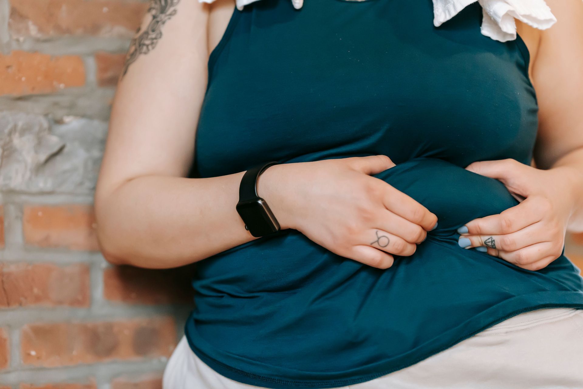 Person resting hands on a teal shirt against a brick wall.