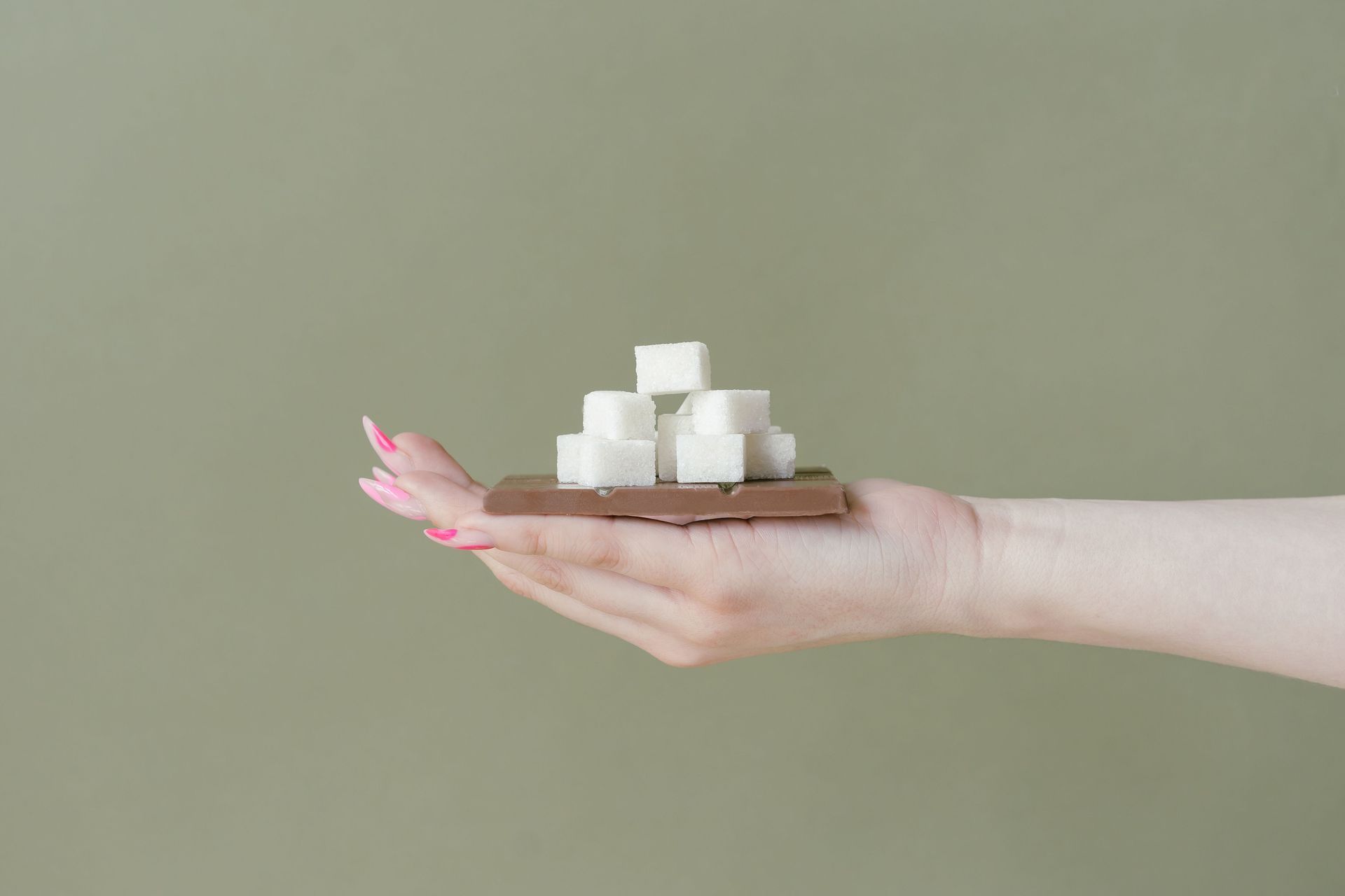 Hand holding stacked white sugar cubes against a muted green background