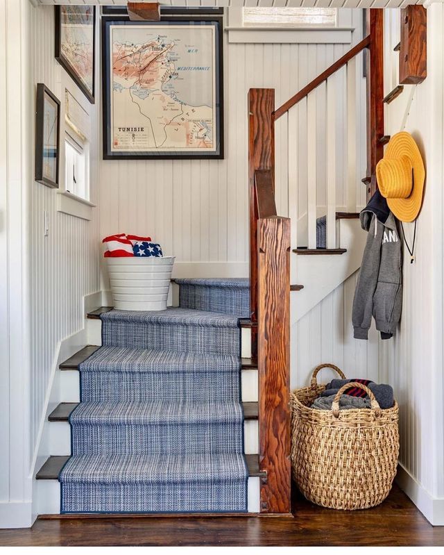 Cozy entryway with blue-carpeted stairs, woven basket, framed map, and hanging hats on wood hooks