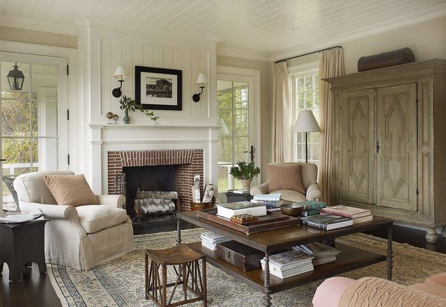 Cozy living room with fireplace, cream chairs, wooden coffee table, and large armoire near bright windows