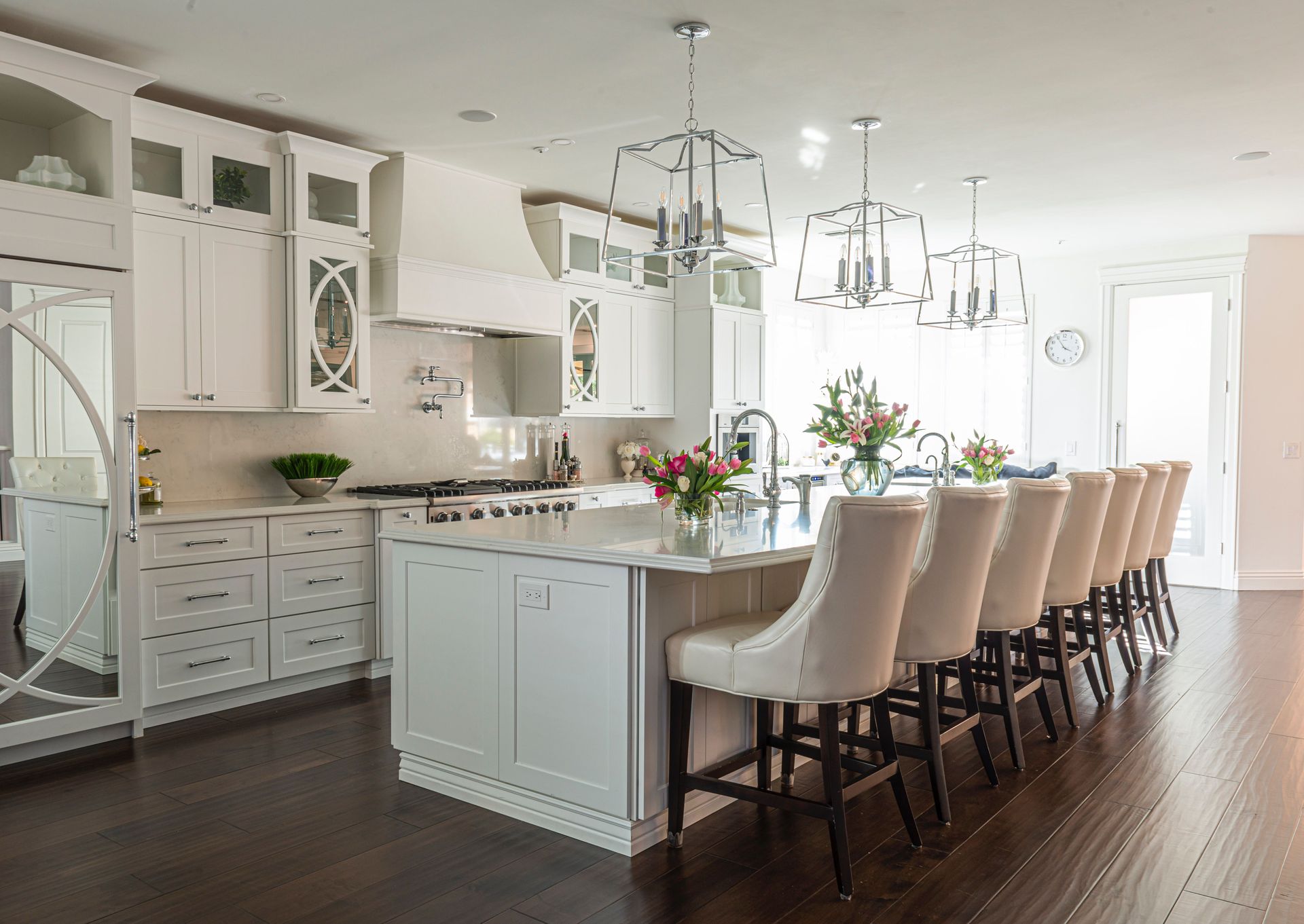 Bright white kitchen with long island, bar stools, pendant lights, and dark wood floors