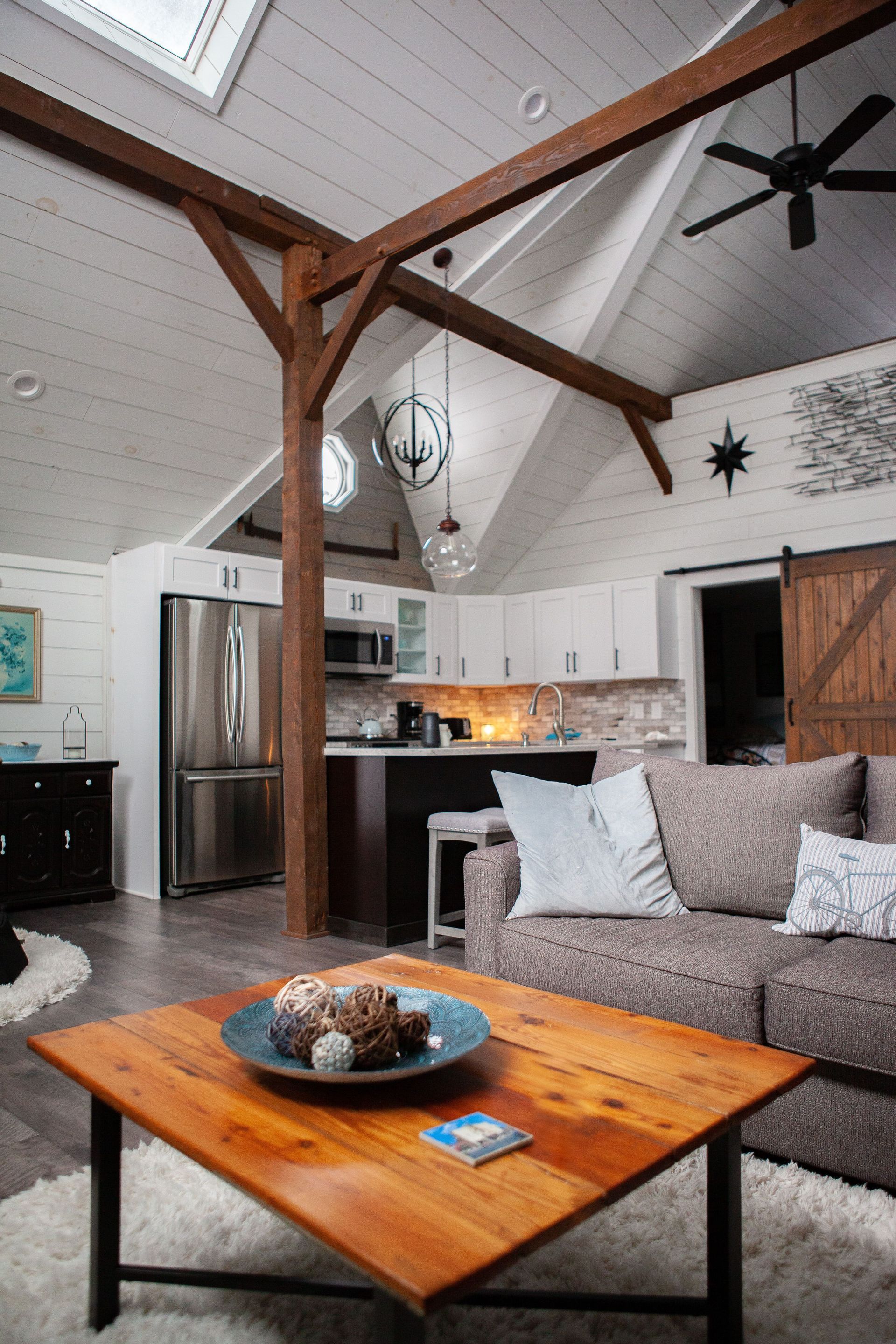 Cozy living room with vaulted ceiling, gray sofa, wood coffee table, and kitchen in the background