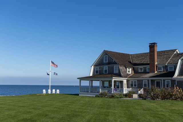 Coastal house with flagpole on a grassy lawn beside the ocean under a clear blue sky