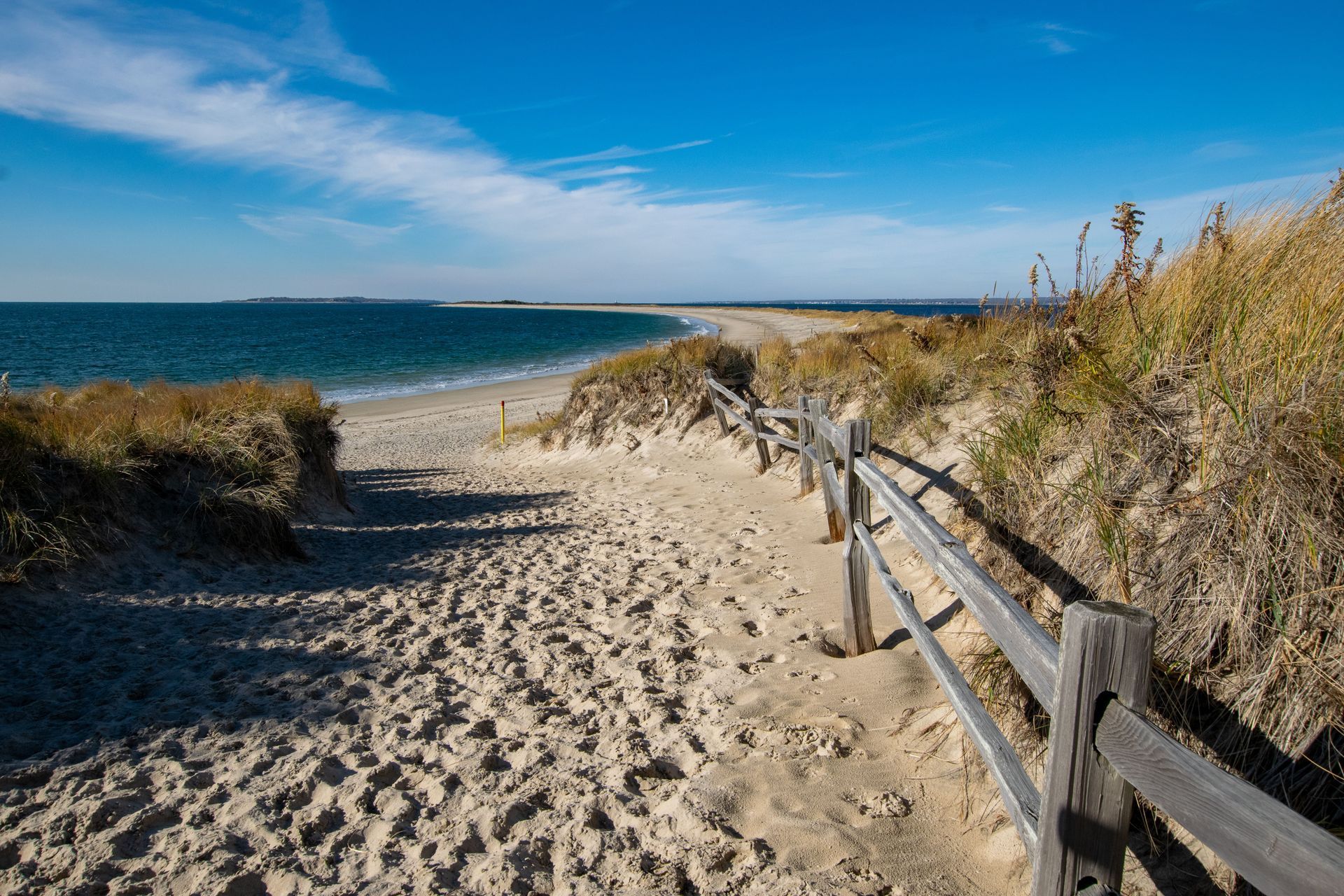 Sandy beach path beside wooden fence leading to blue ocean under a clear sky