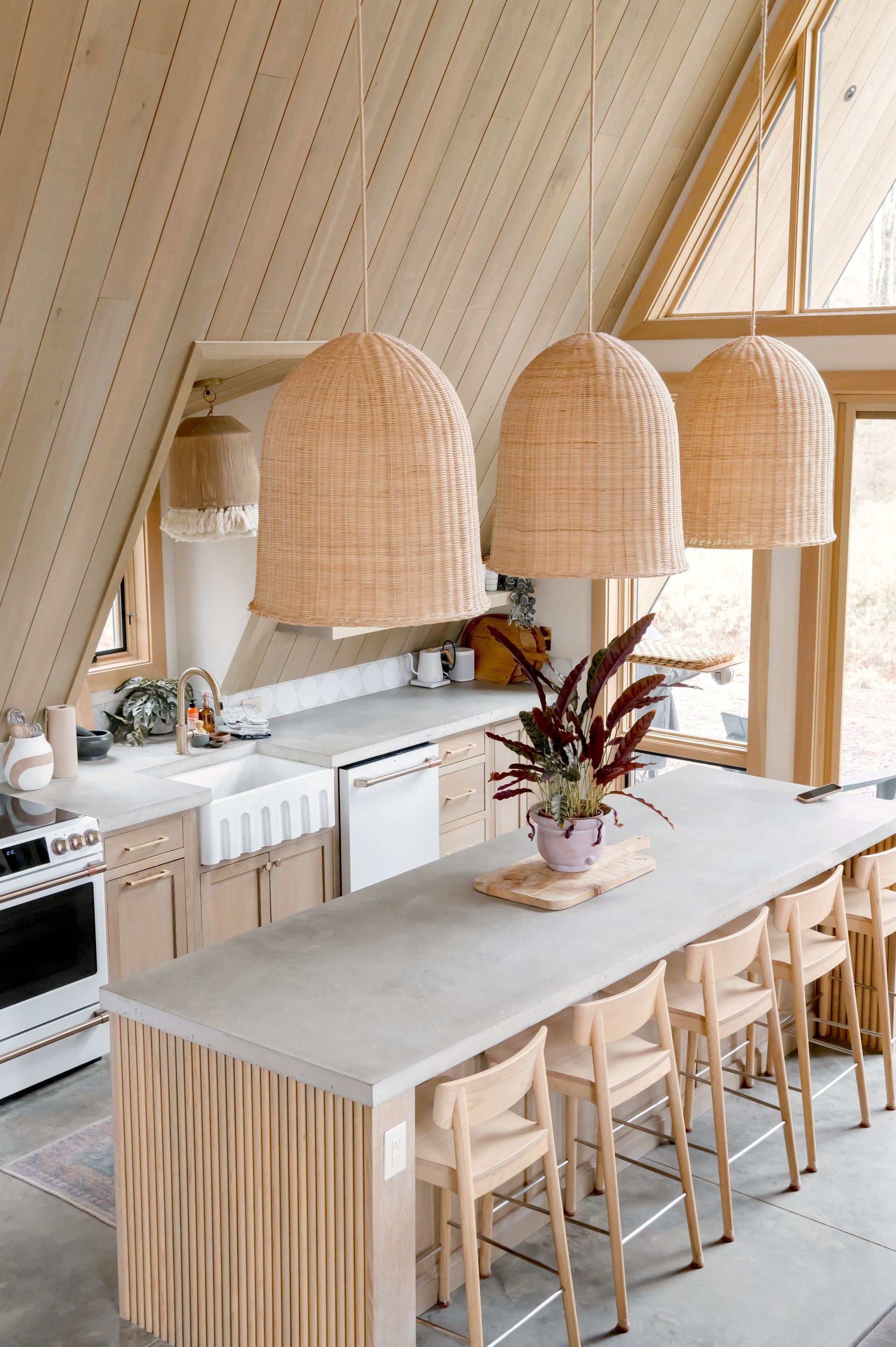 Modern kitchen with a long island, woven pendant lights, and wooden stools under a sloped ceiling