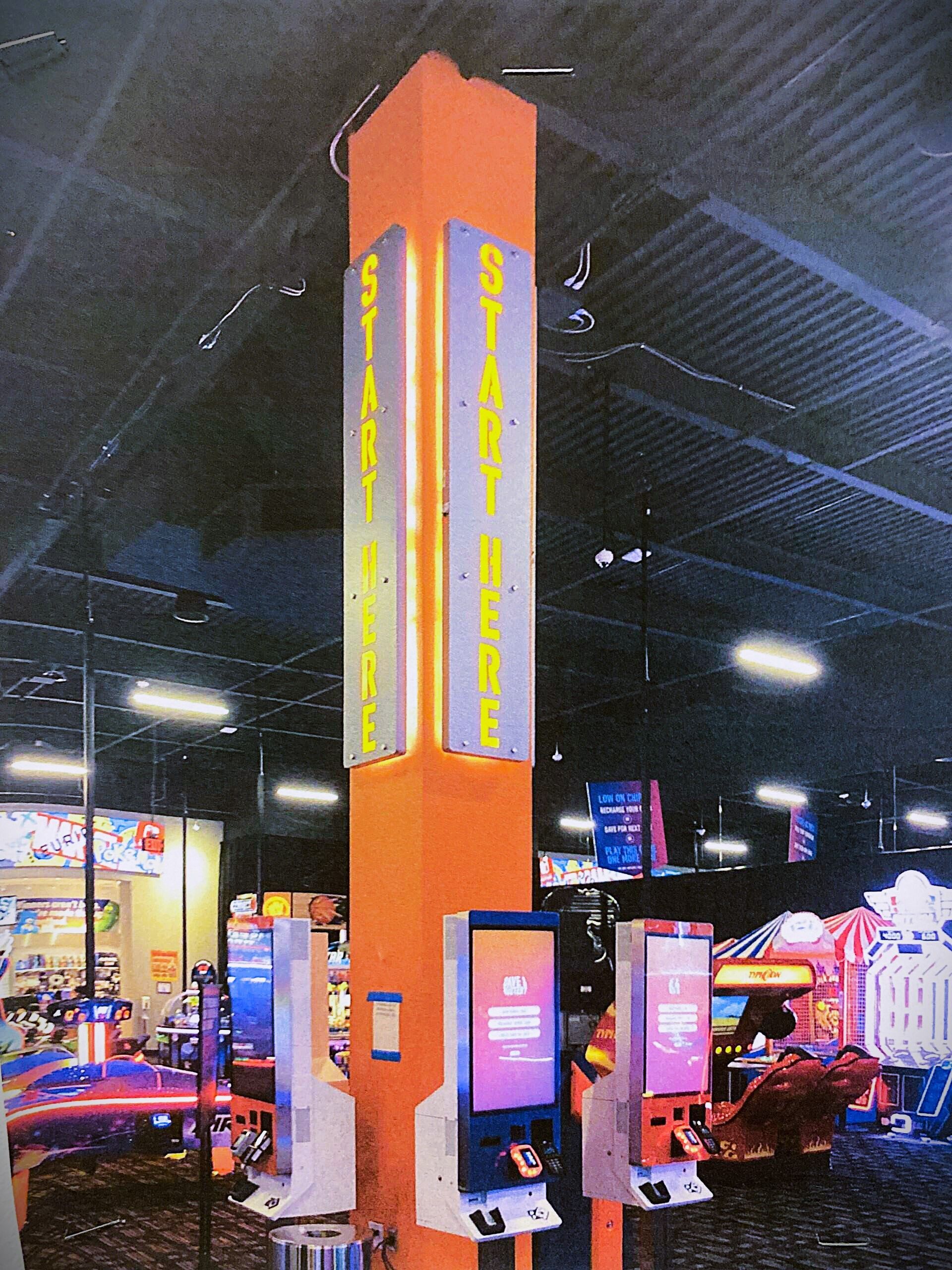 Tall orange arcade kiosk with glowing screens in a dimly lit game room