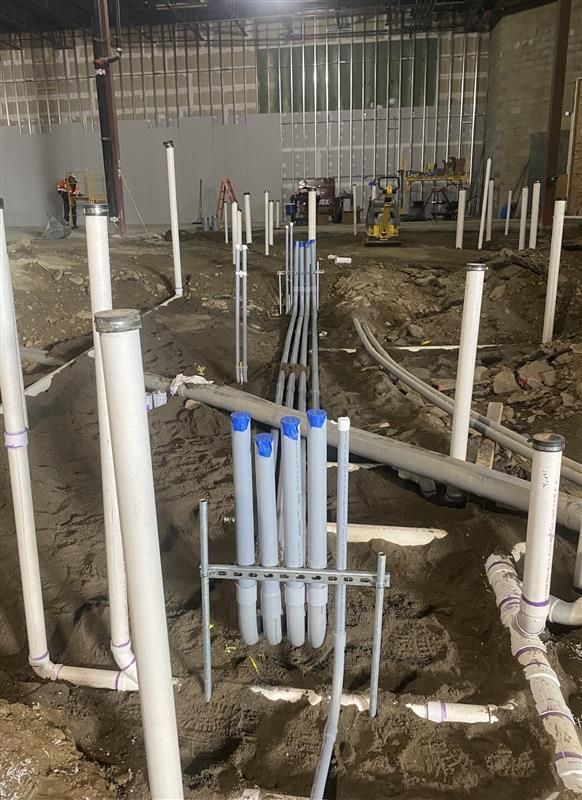 Construction site with exposed pipes and plumbing lines in a dirt floor room