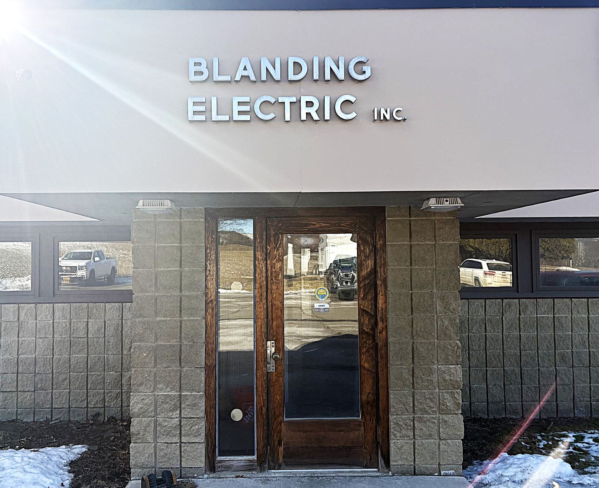 Exterior of Blanding Electric Inc. storefront with tan awning, glass doors, and brick walls
