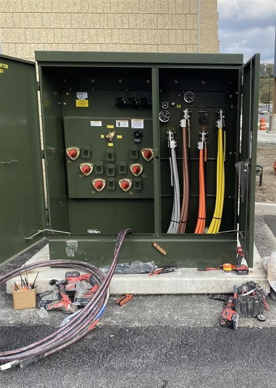 Open electrical control cabinet with switches, gauges, and cables outside beside a building