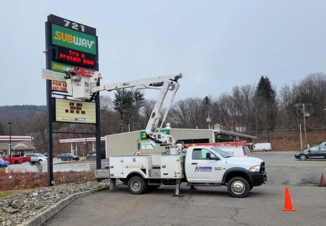 Utility truck with bucket lift beside a shopping plaza sign in a parking lot