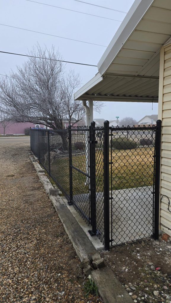 Chain-link fence beside a beige house along a gravel yard under a cloudy sky