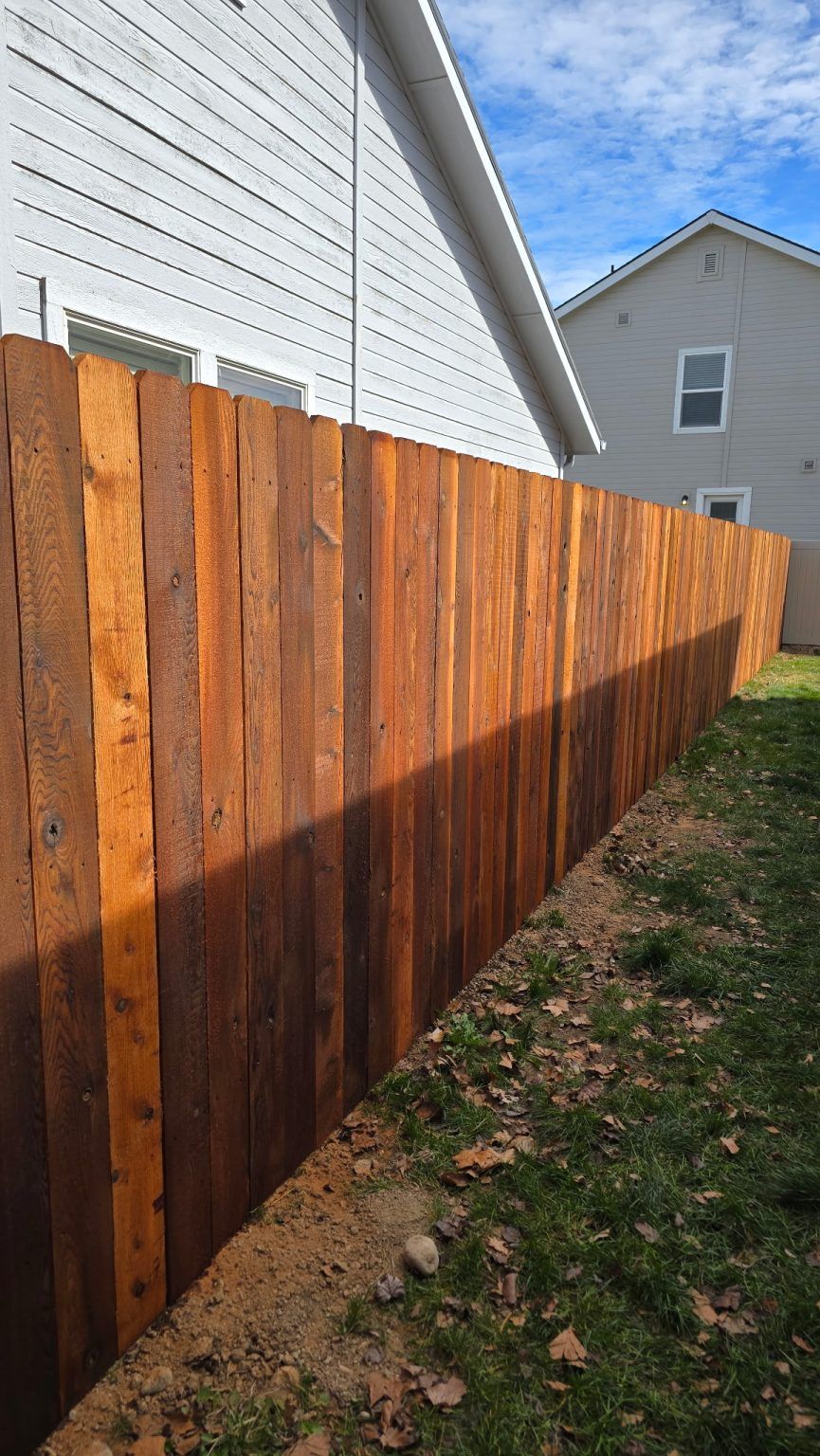 Freshly stained wooden fence along a narrow yard beside a white house, with another house in the background