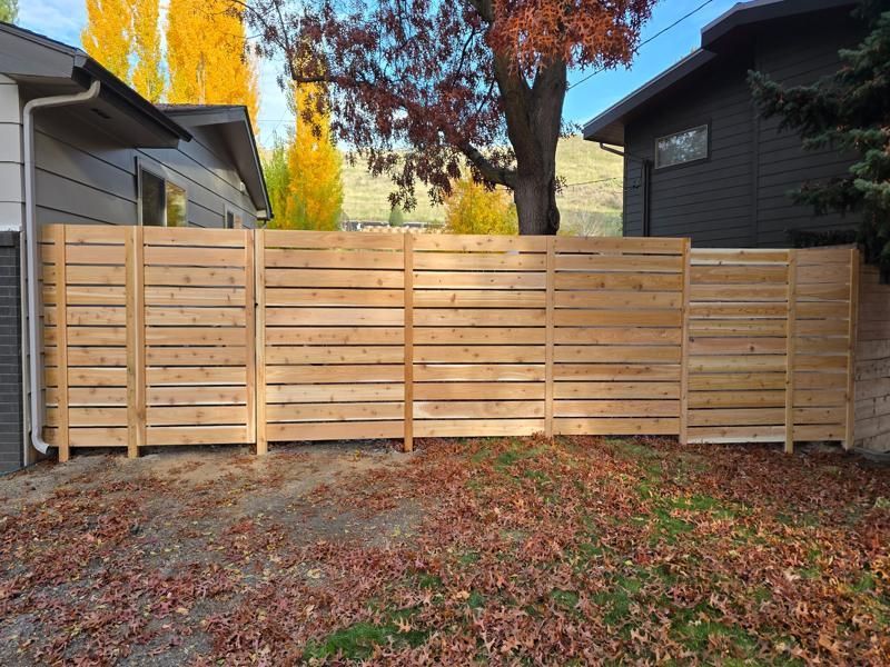 Wooden privacy fence across a backyard with fallen autumn leaves and neighboring houses visible behind it