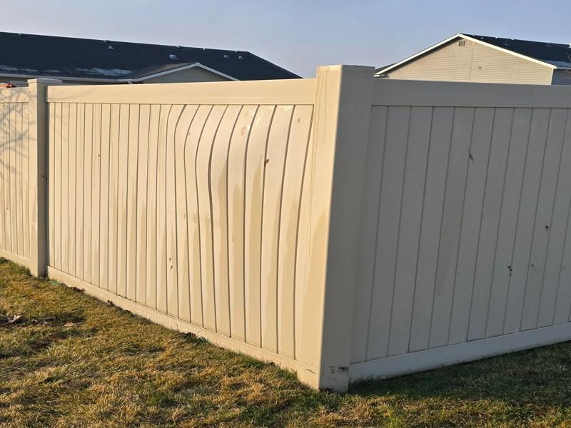 White vinyl fence with a wavy panel beside a beige fence in a suburban yard