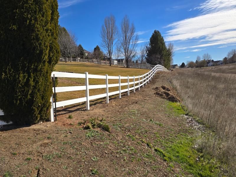 White fence along a dirt path beside a grassy field under a blue sky