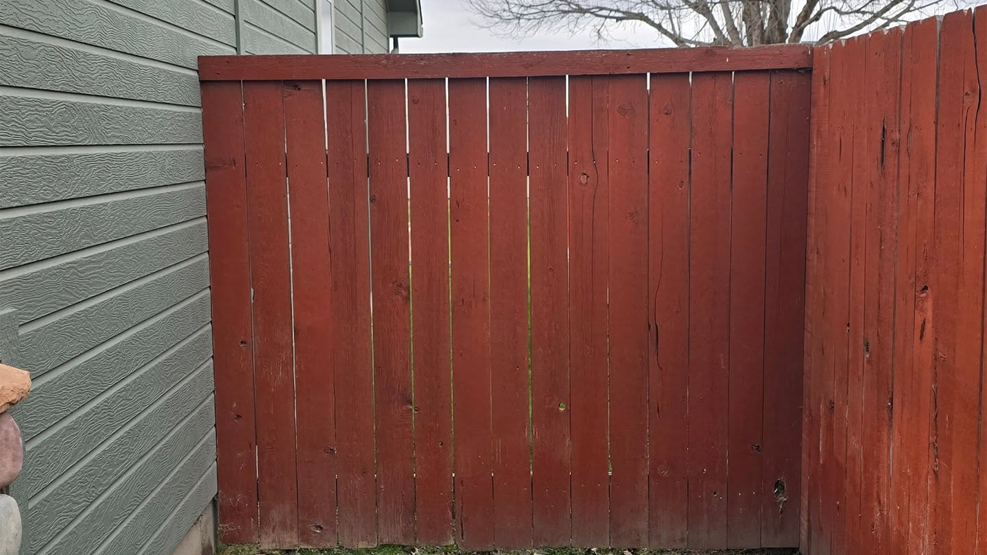 Red wooden fence with a gate beside a gray brick wall in an outdoor yard