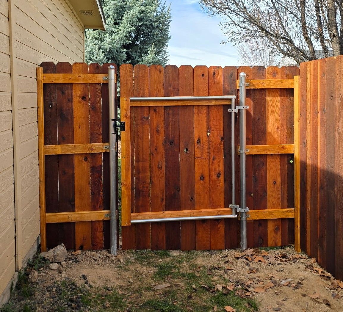 Wooden backyard gate with metal crossbars and latch, set between fence panels and a house wall.
