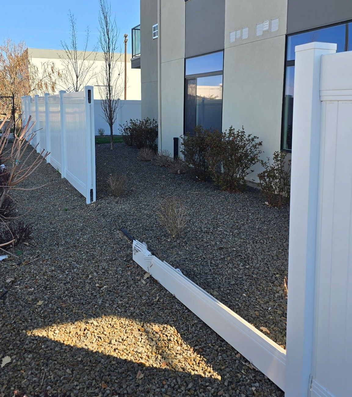 White fence posts and a fallen rail beside a beige building in a gravel yard.