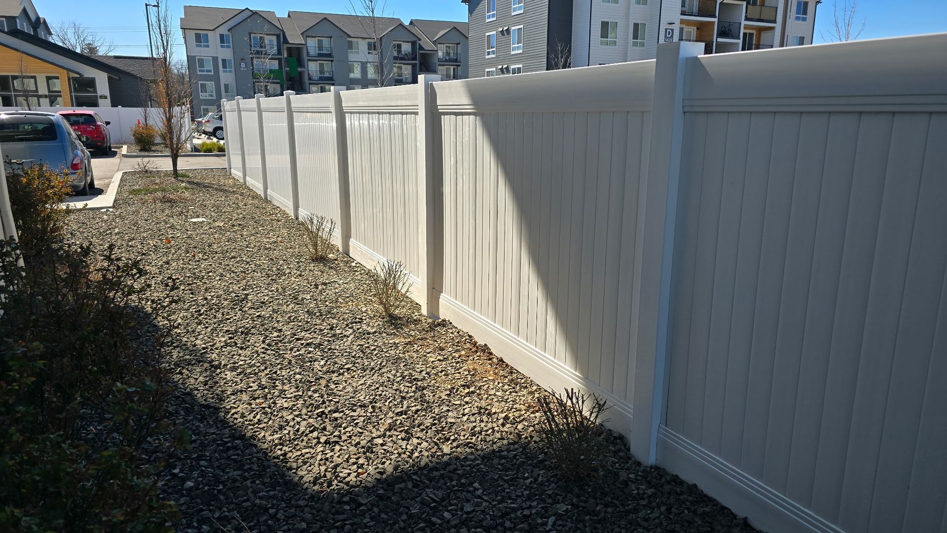 White vinyl fence beside a gravel strip along a residential sidewalk on a sunny day