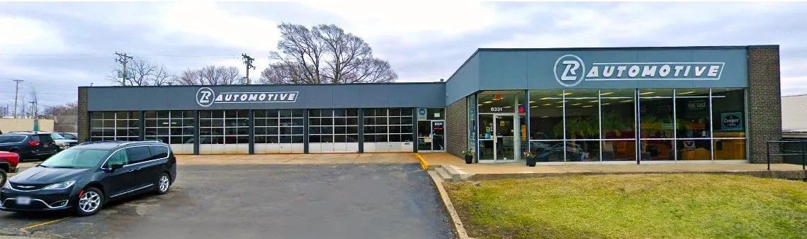 Strip mall storefronts with a parked dark car in front and a grassy verge on the right