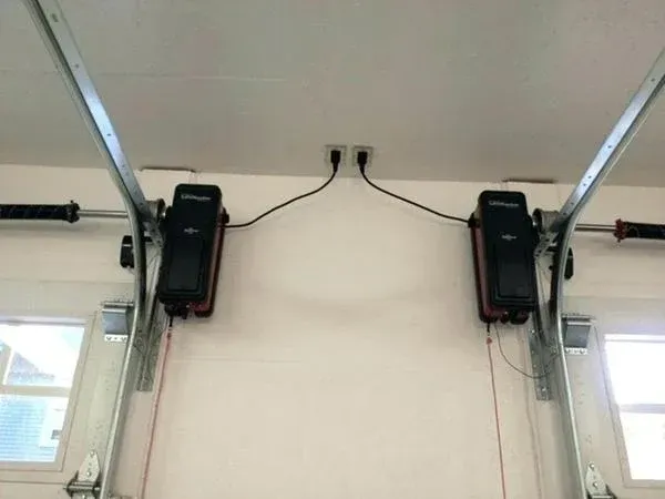 Garage ceiling with two wall-mounted black garage door openers and hanging rails above windows