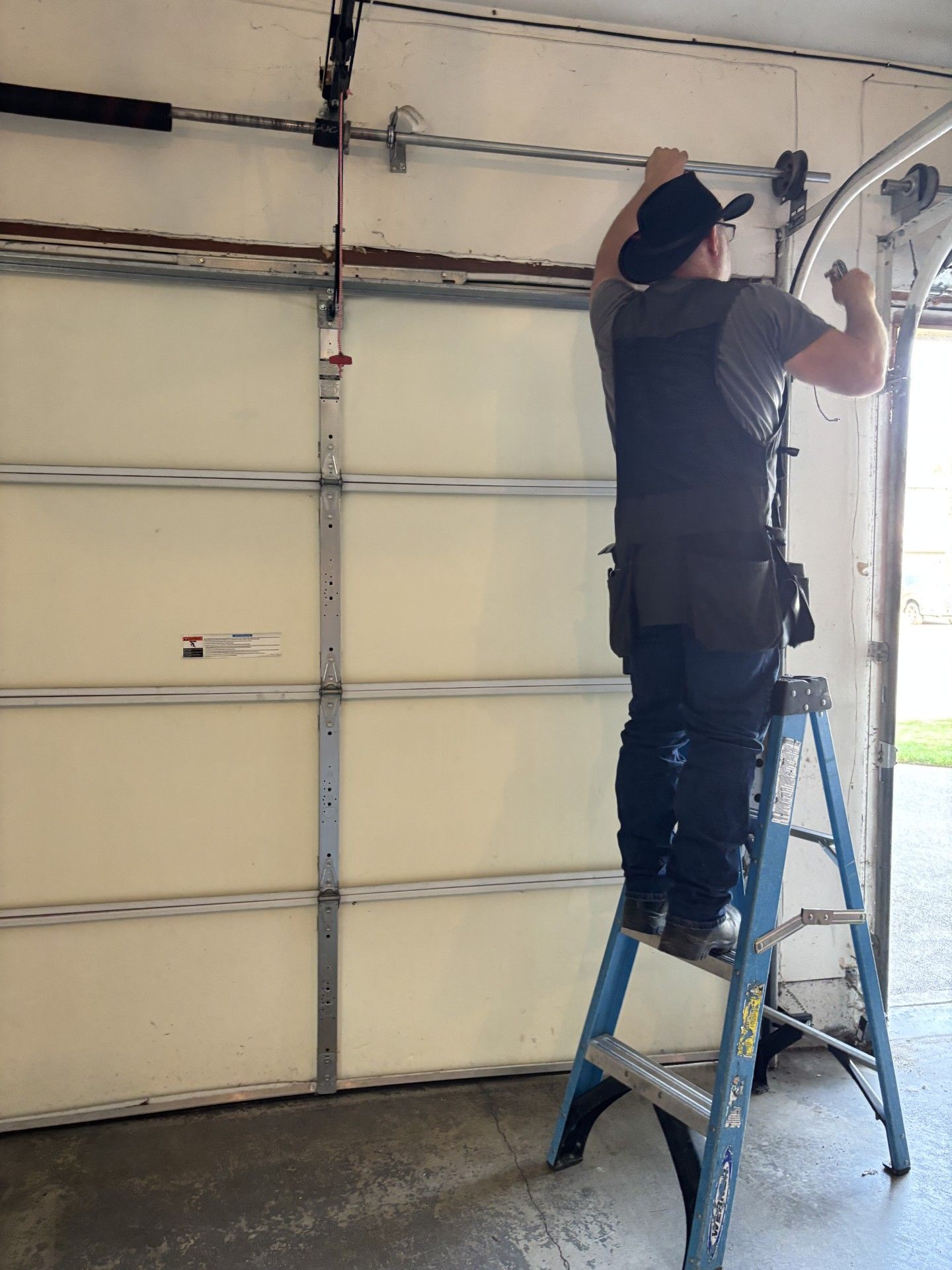 Person on a blue ladder working on a garage door opener mechanism.