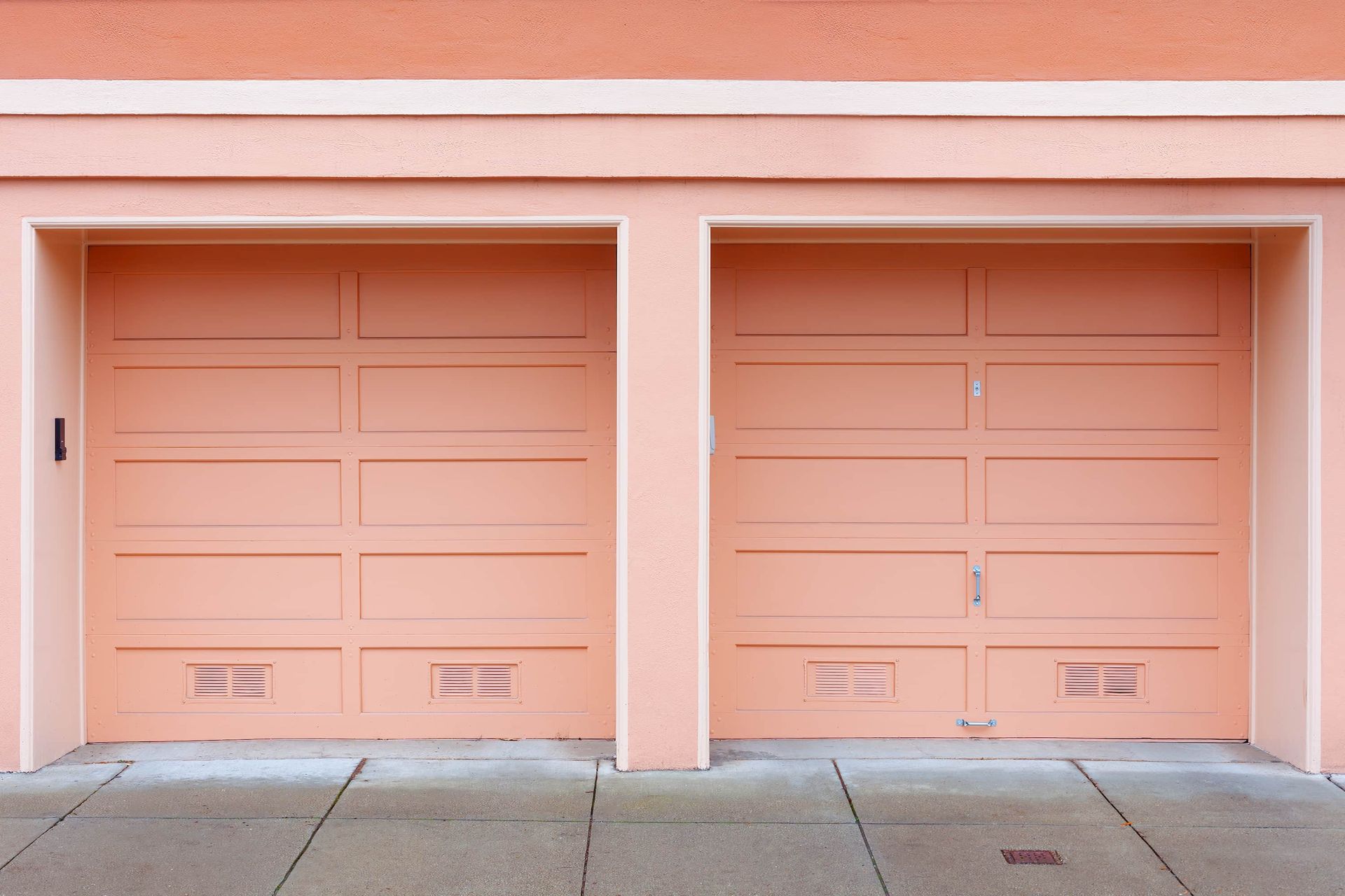 Two peach-colored garage doors in a pink stucco building facade