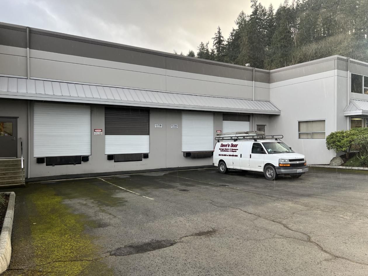 Small industrial building with roll-up doors and a white service van parked outside on a wet lot