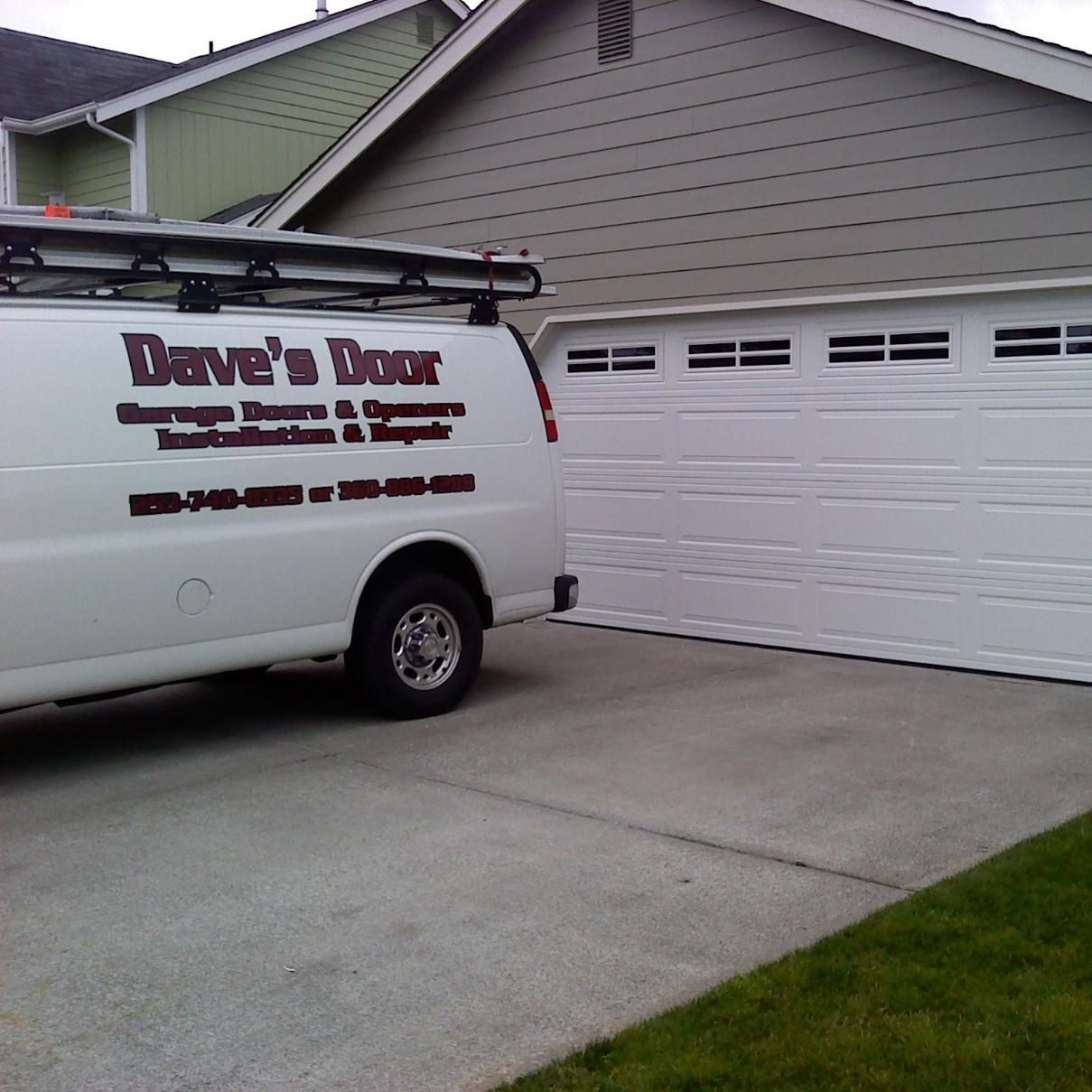 White service van parked in a driveway beside a gray garage with a green-roofed house in the background