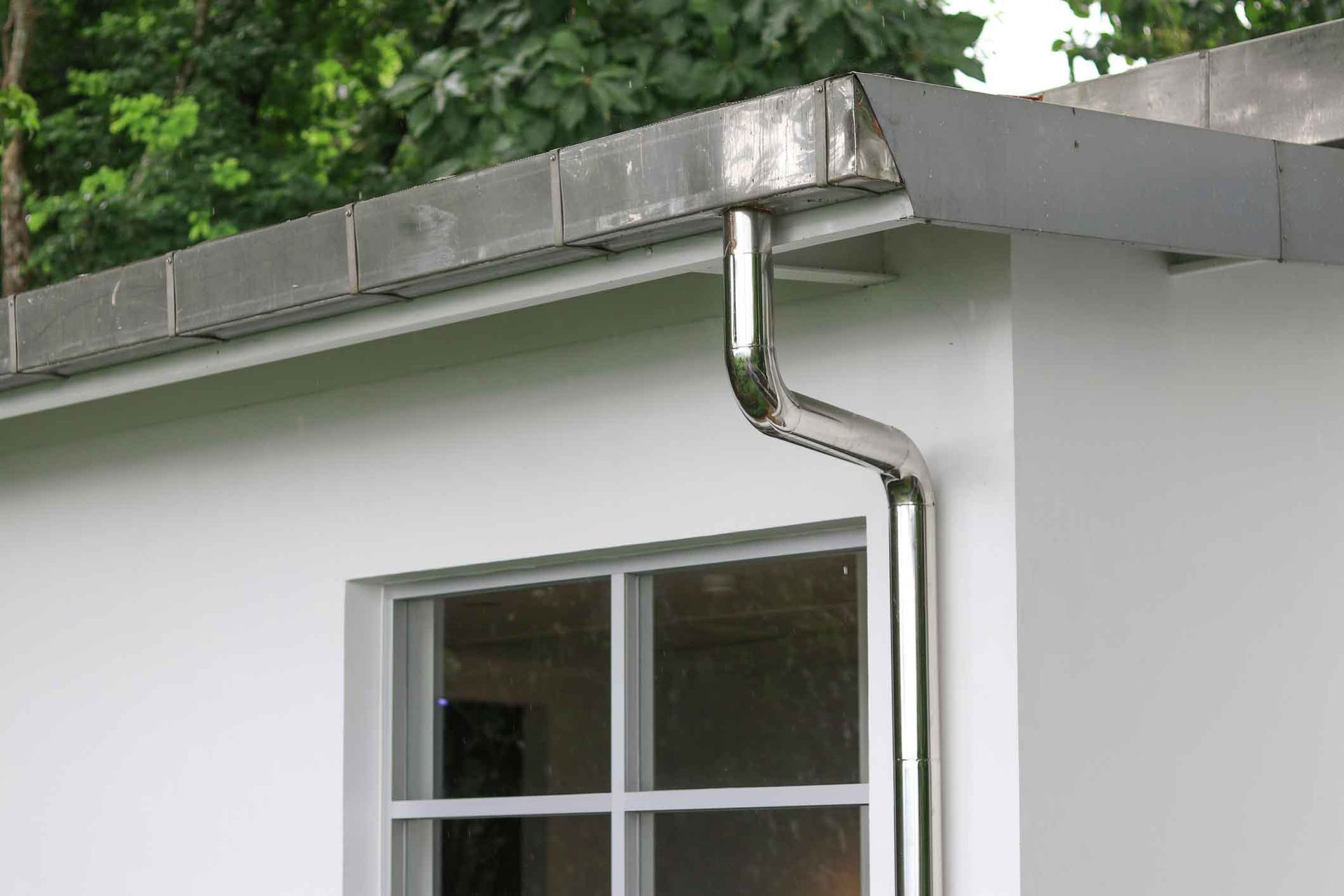A gutter on the side of a white building next to a window.