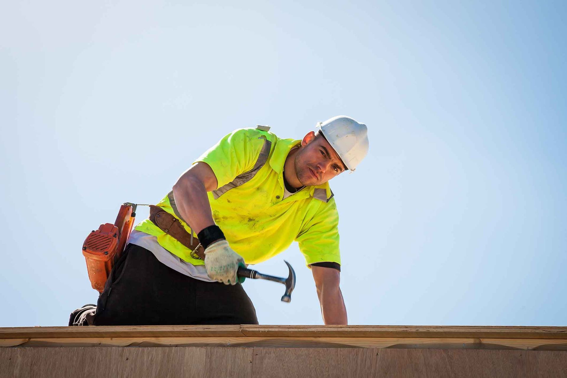 A man is kneeling on a roof holding a hammer.